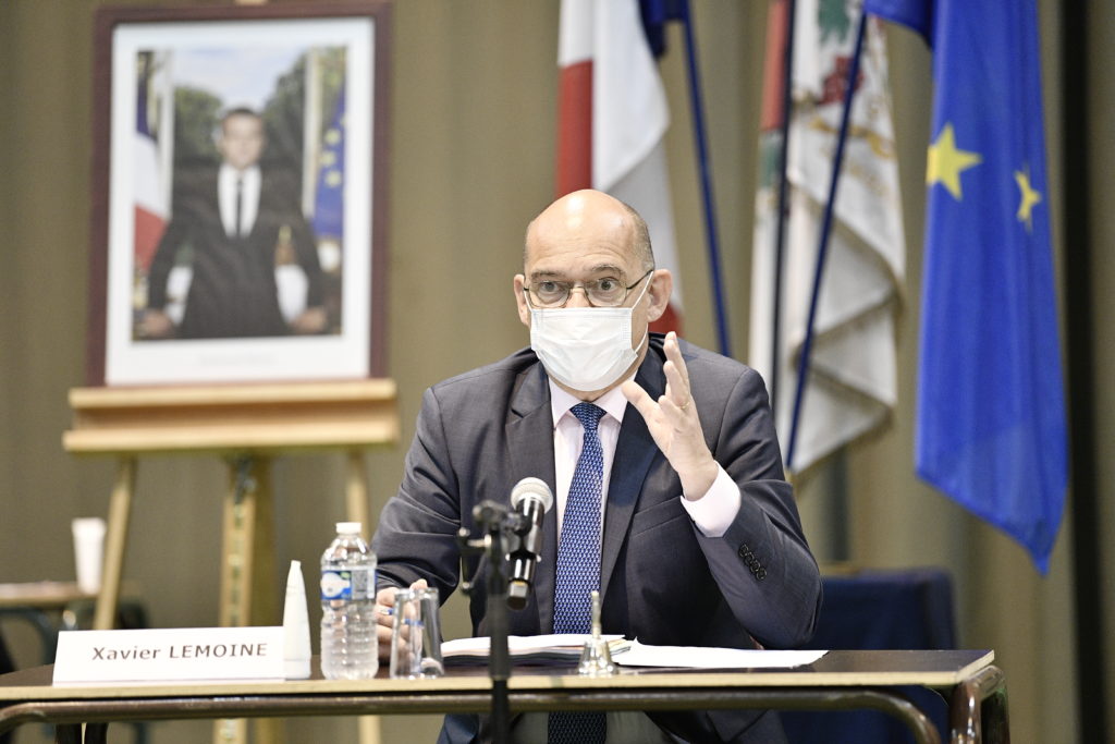 Xavier Lemoine avec un masque avec un tableau et des drapeaux en arrière plan